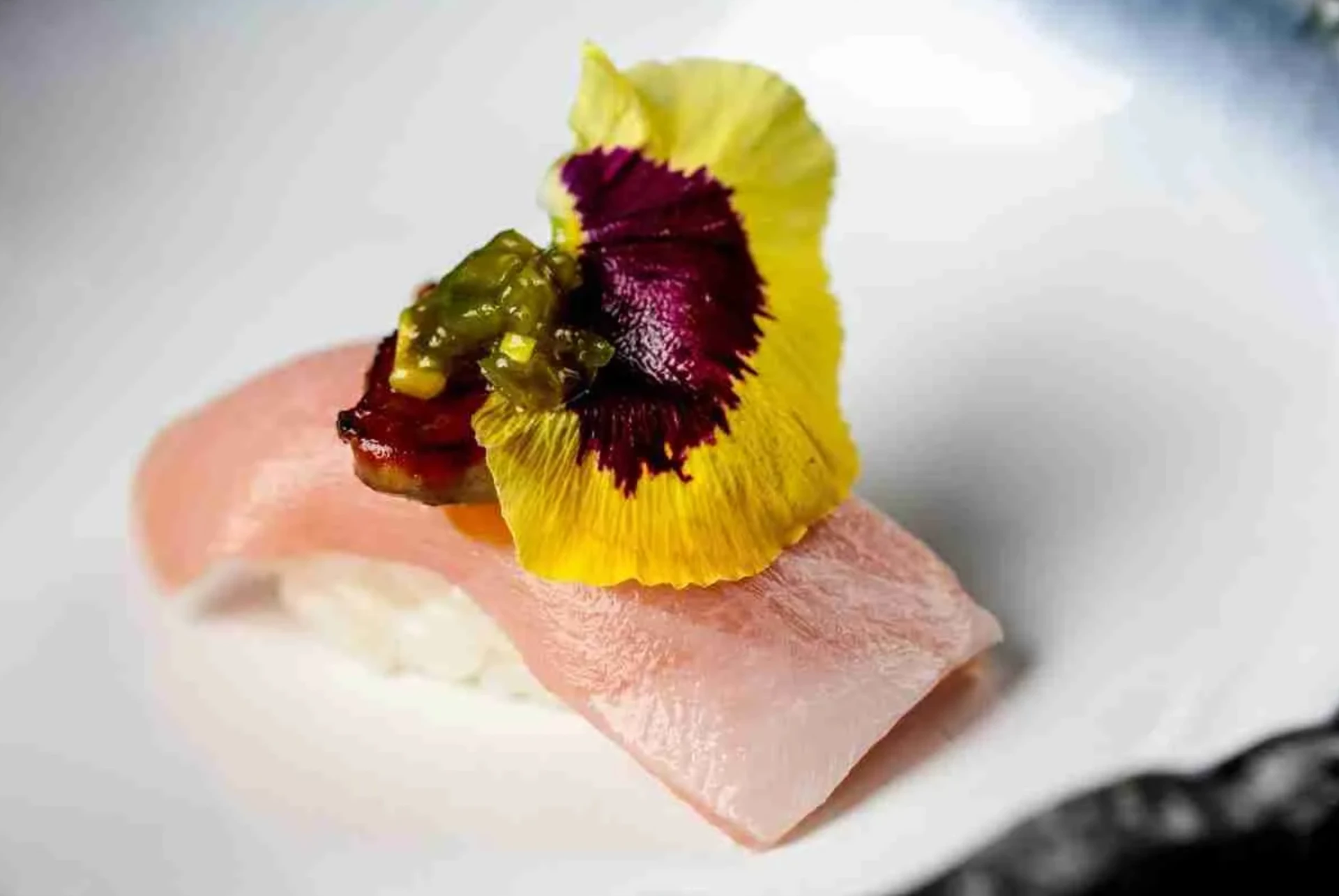 Nigiri topped with an edible yellow pansy and yuzu relish on a white plate