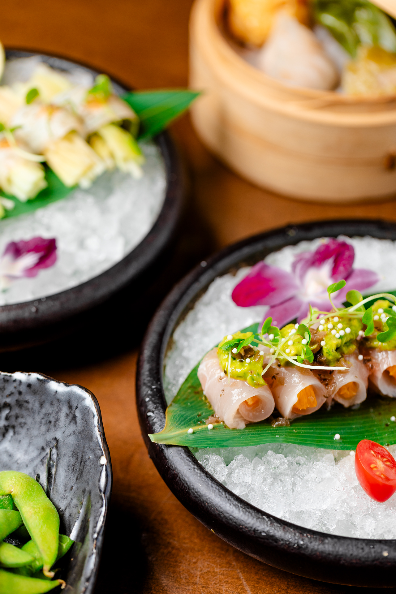 Yellowtail crudo rolls with citrus, avocado and edible flowers served on crushed ice in black bowls